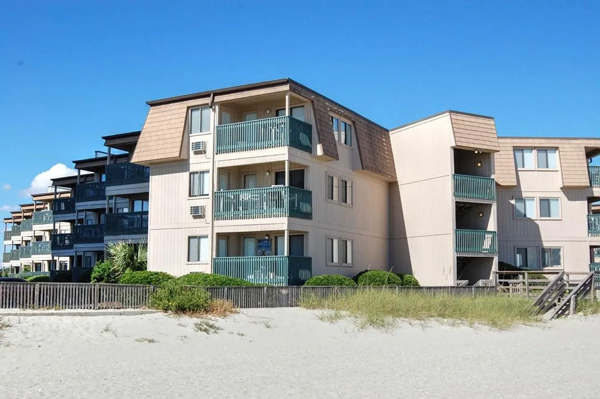 A beachfront property with several balconies overlooking the soft sand and ocean, framed by lush landscaping. The scene invites families to imagine stepping right from their accommodations onto the beach for outings or relaxation. The morning sunlight enhances the warmth and openness of the setting, hinting at the ease of access to both the beach and resort amenities.