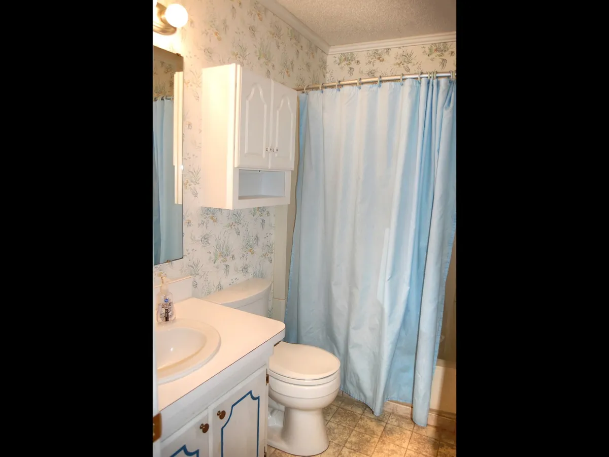 A tranquil bathroom with a sink and mirror, blue shower curtain, vanity unit, and floral wallpaper. The soothing color palette and thoughtful details create a relaxing space for self-care rituals.