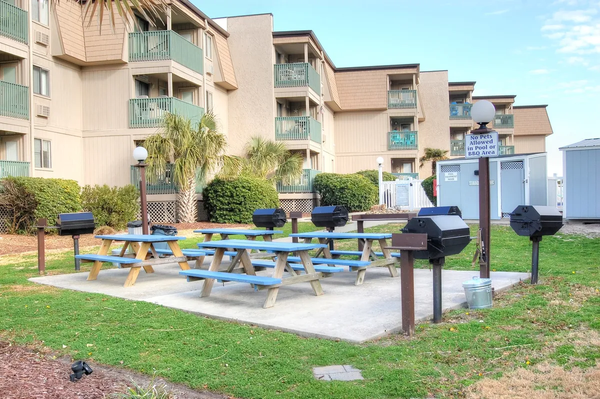 The scene shows picnic tables and barbecue grills nestled among lush greenery, providing an inviting space for outdoor meals and social gatherings. It conveys an atmosphere of community and highlights spaces where guests can grill, dine, and interact.