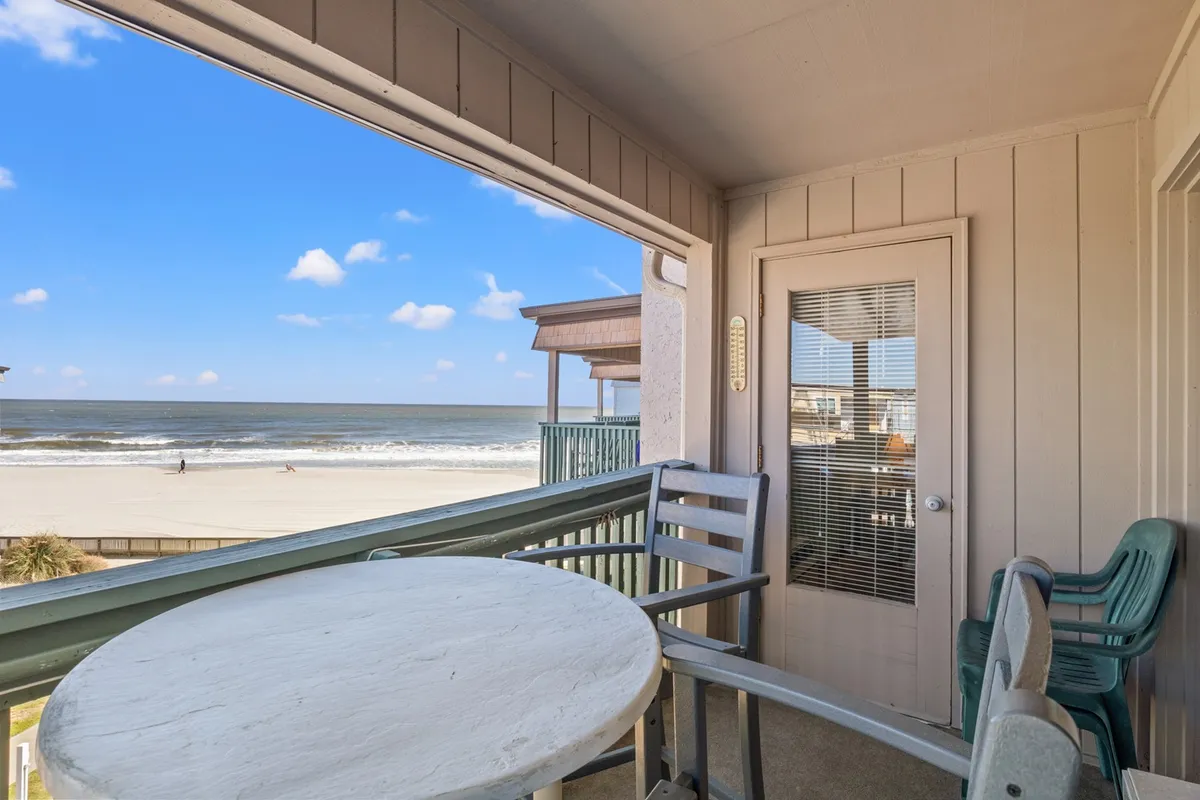 An exterior view from the balcony overlooking the ocean, with outdoor seating and coastal decor inviting guests to enjoy morning coffee, evening cocktails, or simply soak up the tranquil beach scenery.