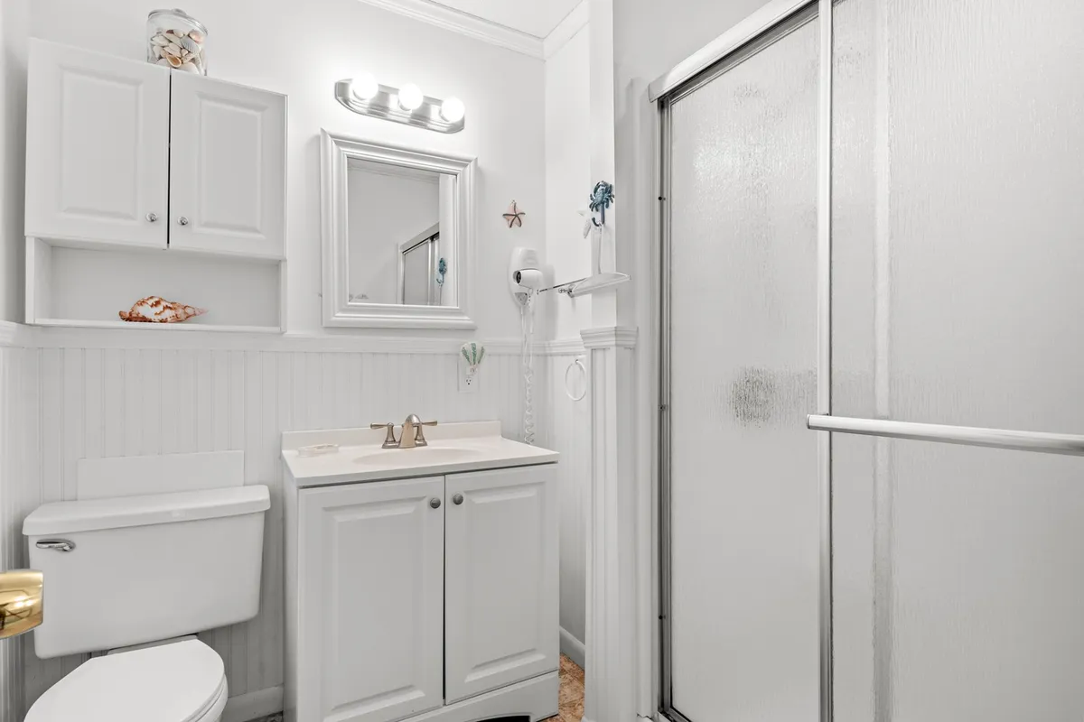 A fresh and inviting bathroom with white cabinetry, a large mirror, a modern shower stall, and bright light fixtures. The clean, uncluttered space is ideal for personal grooming and refreshing showers.
